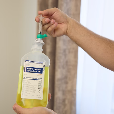 Prikaz boce u kojoj se dodaju vitamini, uz nadzor i stručnost članova tima tokom pripreme infuzije.